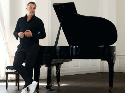 Ein schwarzgekleideter Mann mit weißen Schuhen steht vor einem Flügel