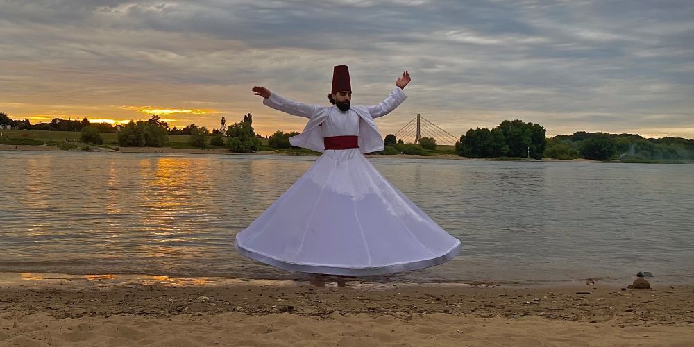 Tänzer in weitem weißen Gewand am Seeufer