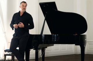 Ein schwarzgekleideter Mann mit weißen Schuhen steht vor einem Flügel