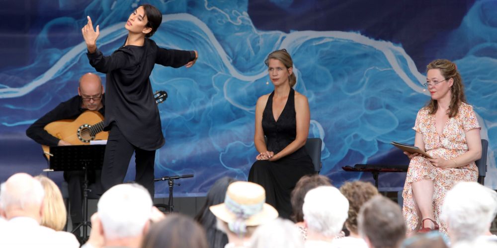 Eine Tänzerin auf der Bühne, im Hintergrund drei Personen