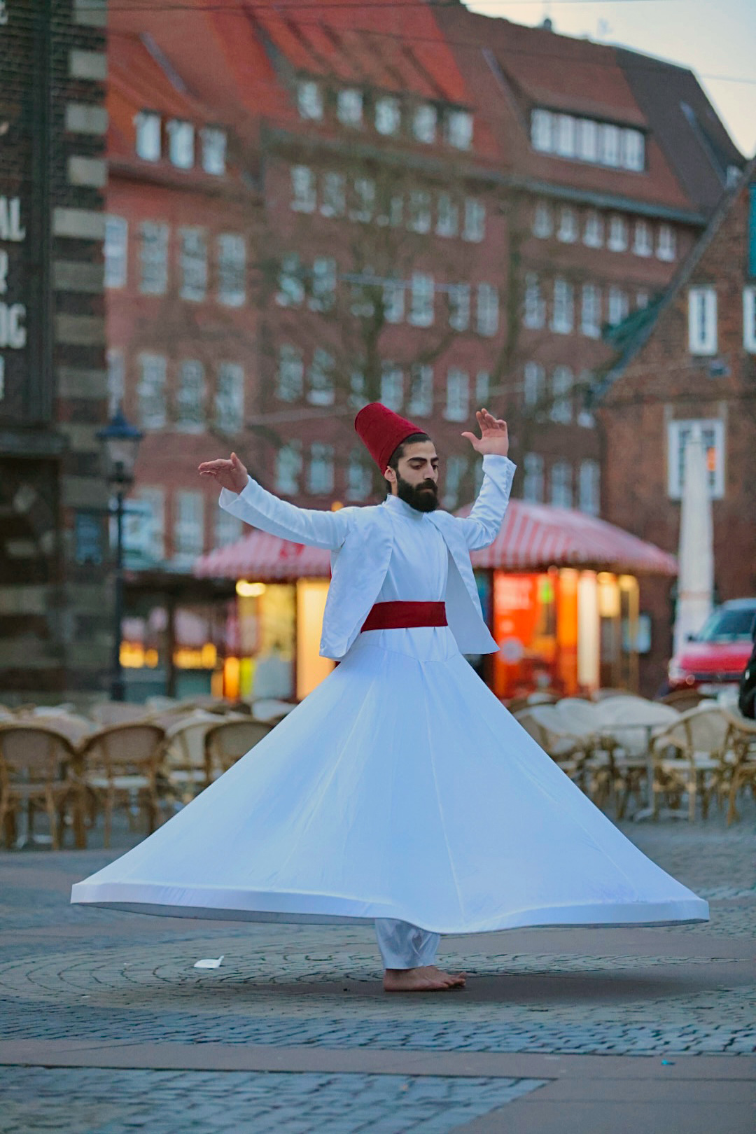 Tänzer in langem weißem Gewand vor städtischen Backsteinhäusern