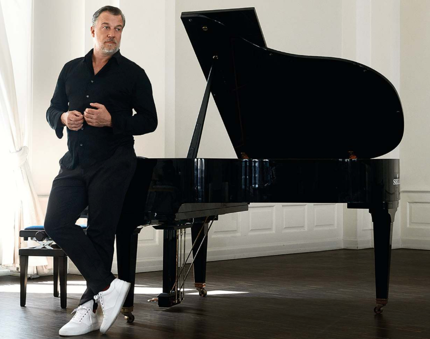 Ein schwarzgekleideter Mann mit weißen Schuhen steht vor einem Flügel